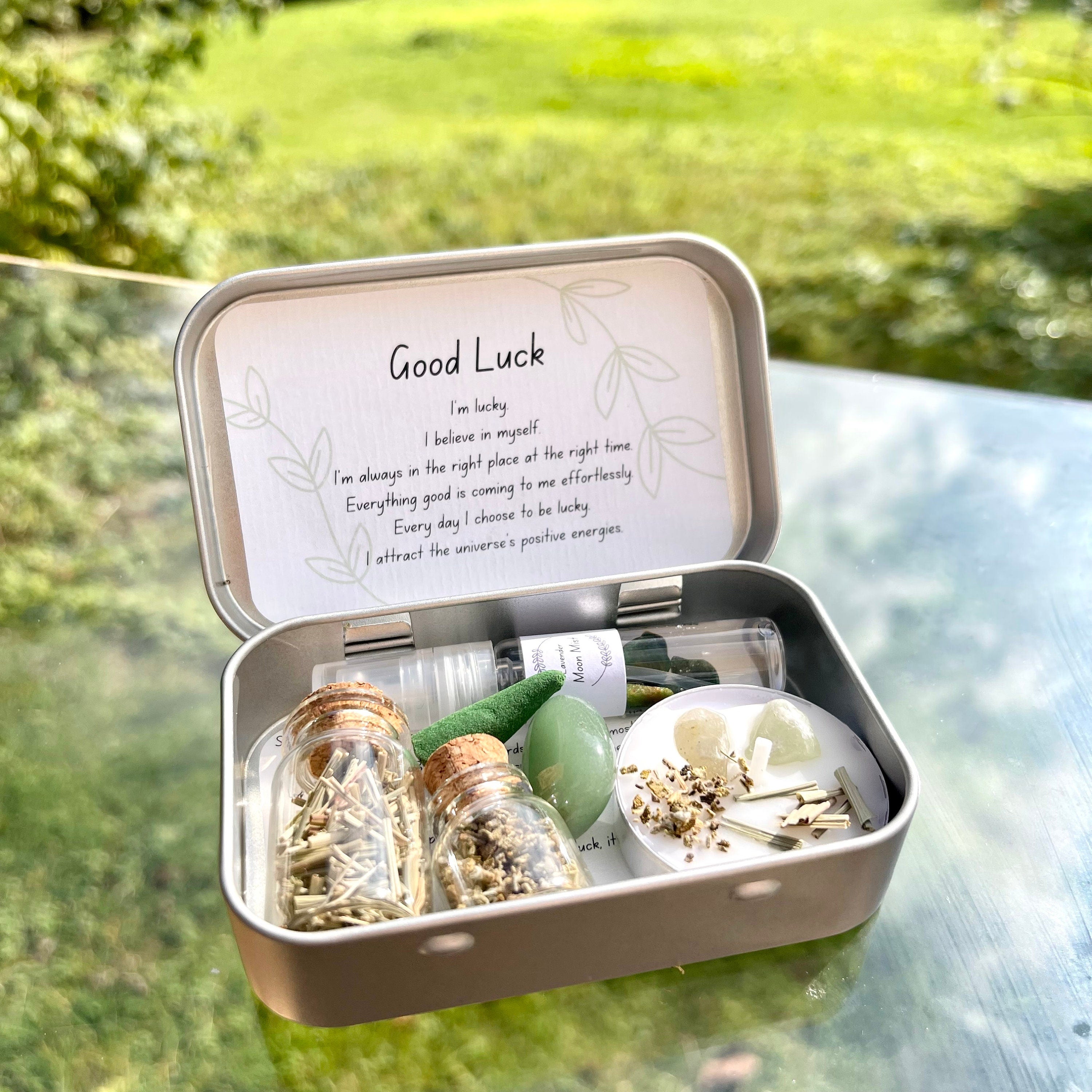 an open metal travel altar tin, inside are 2 jars of herbs, incense, a moon mist, a spell candle and green aventurine tumble stone