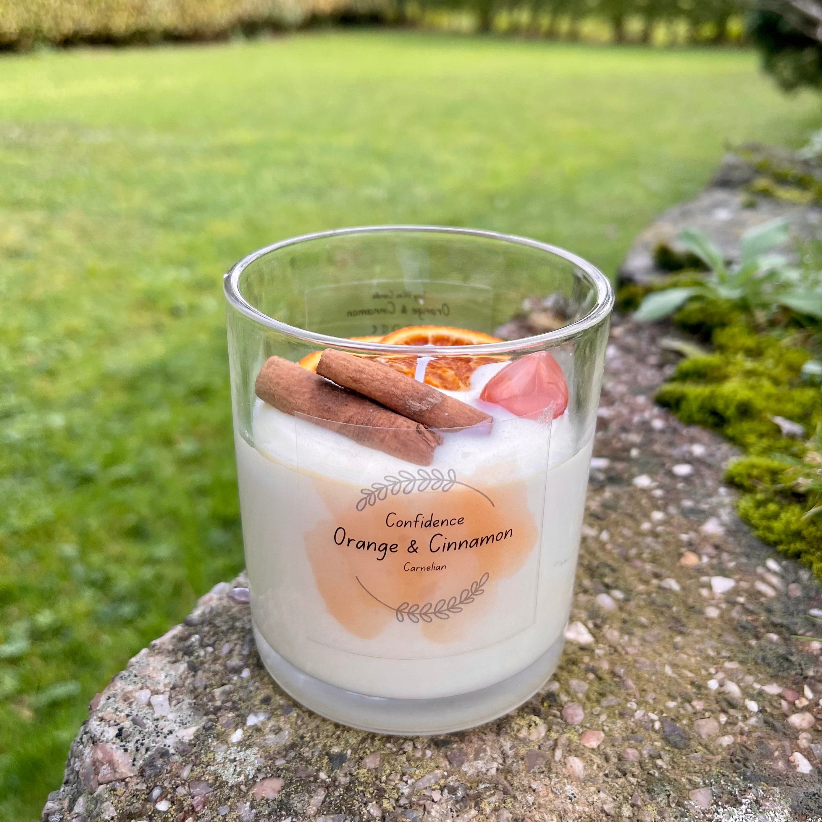 Candle with orange and cinnamon sticks on a stone surface outdoors
