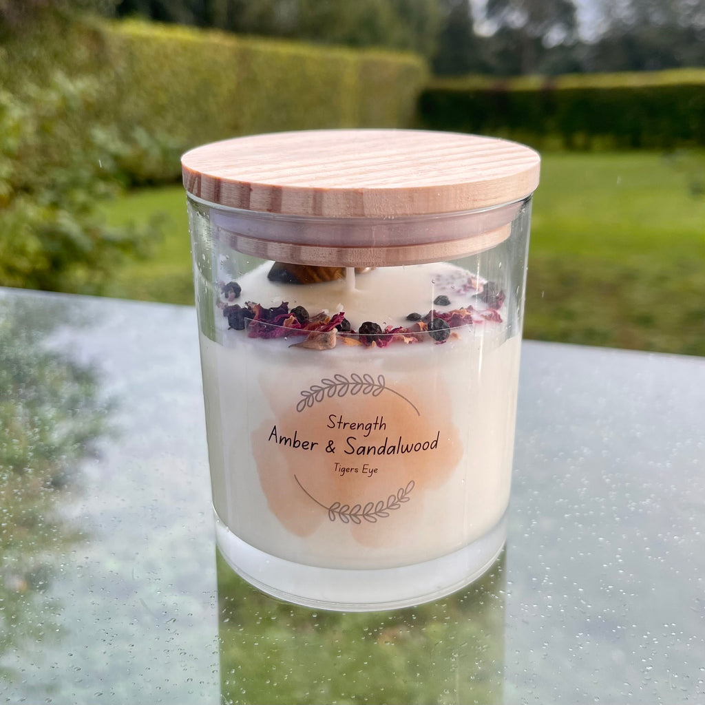A glass jar with white soy wax inside with a tigers eye tumblestone and rose petals set in the top. the jar has a bamboo lid.
