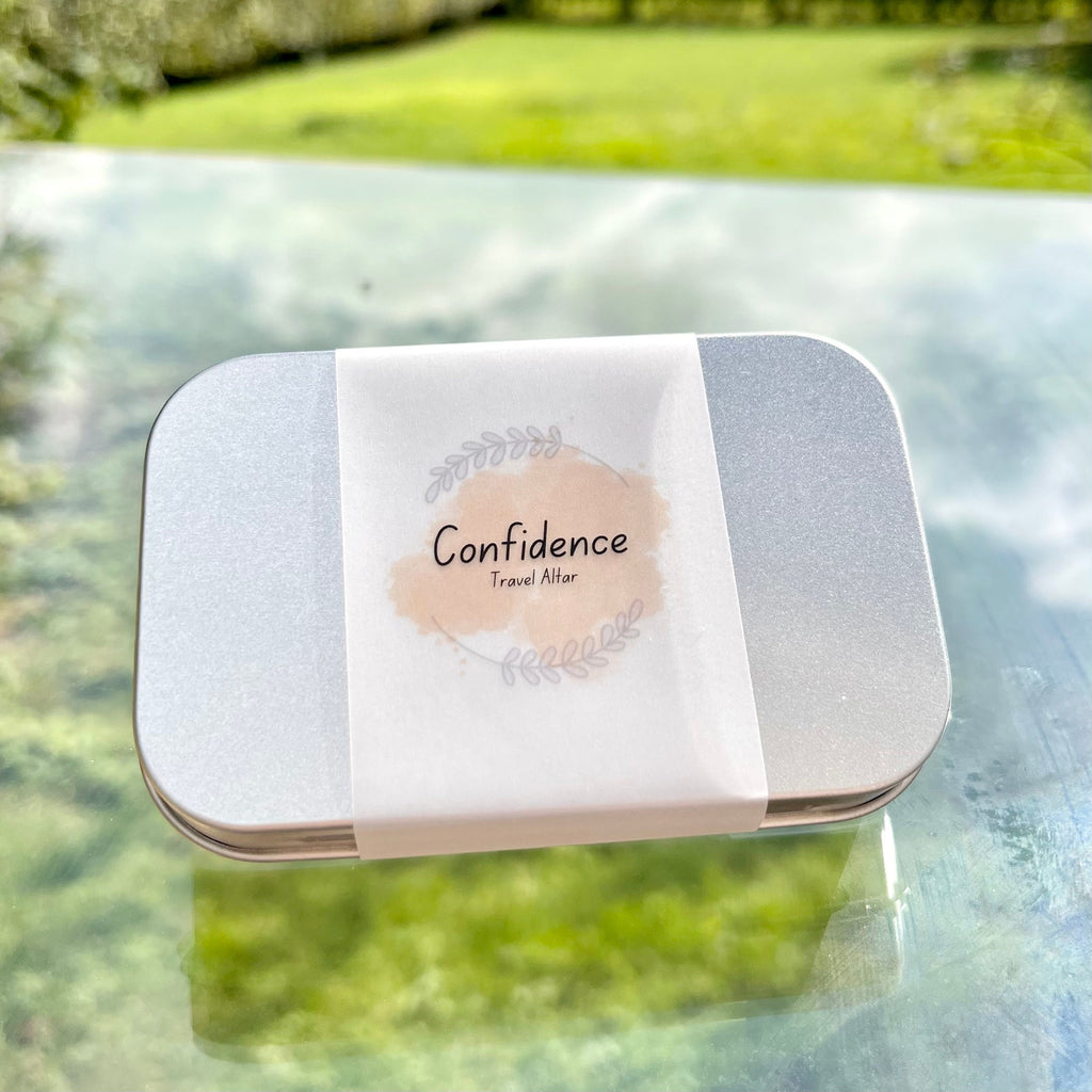 a sealed confidence travel altar in a metal tin and a paper wrap