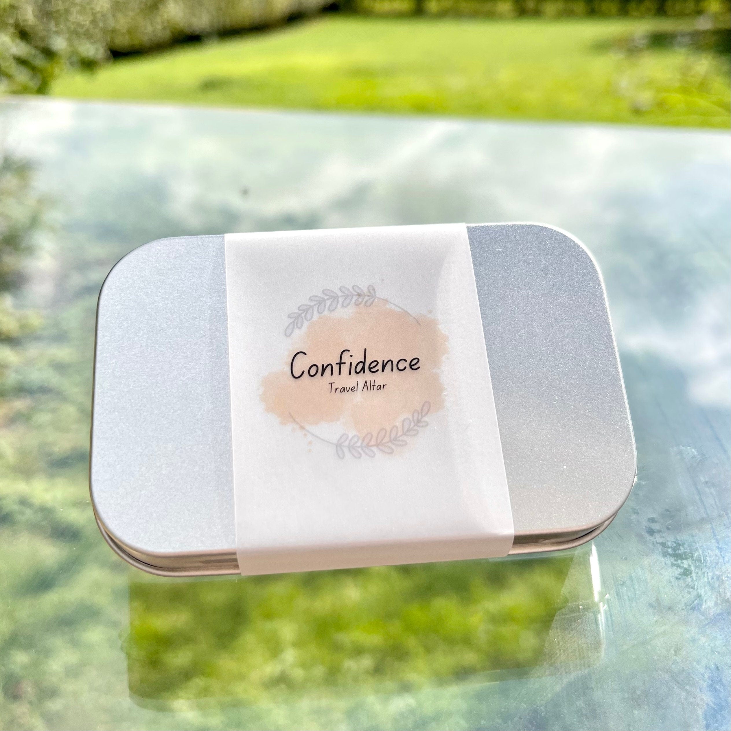 a sealed confidence travel altar in a metal tin and a paper wrap