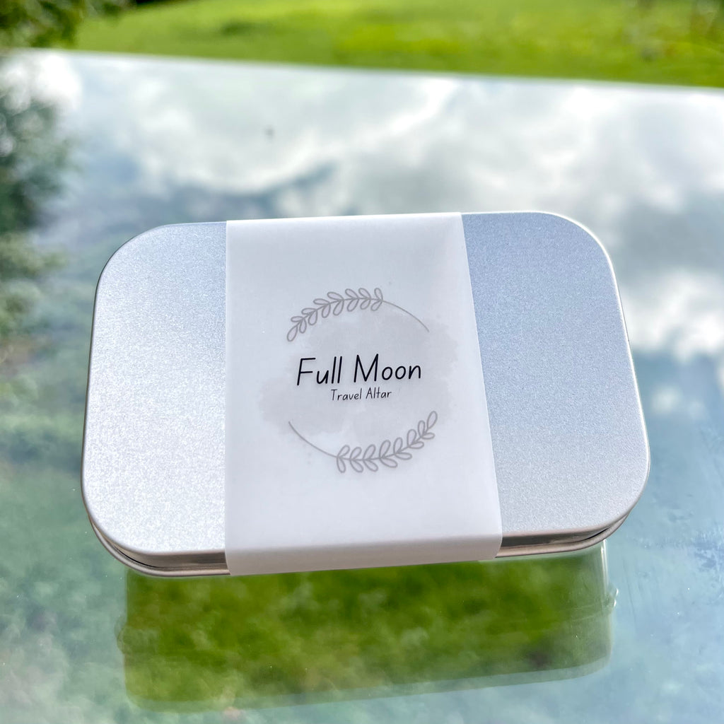 A full moon travel altar. A closed metal tin with a paper wrap.