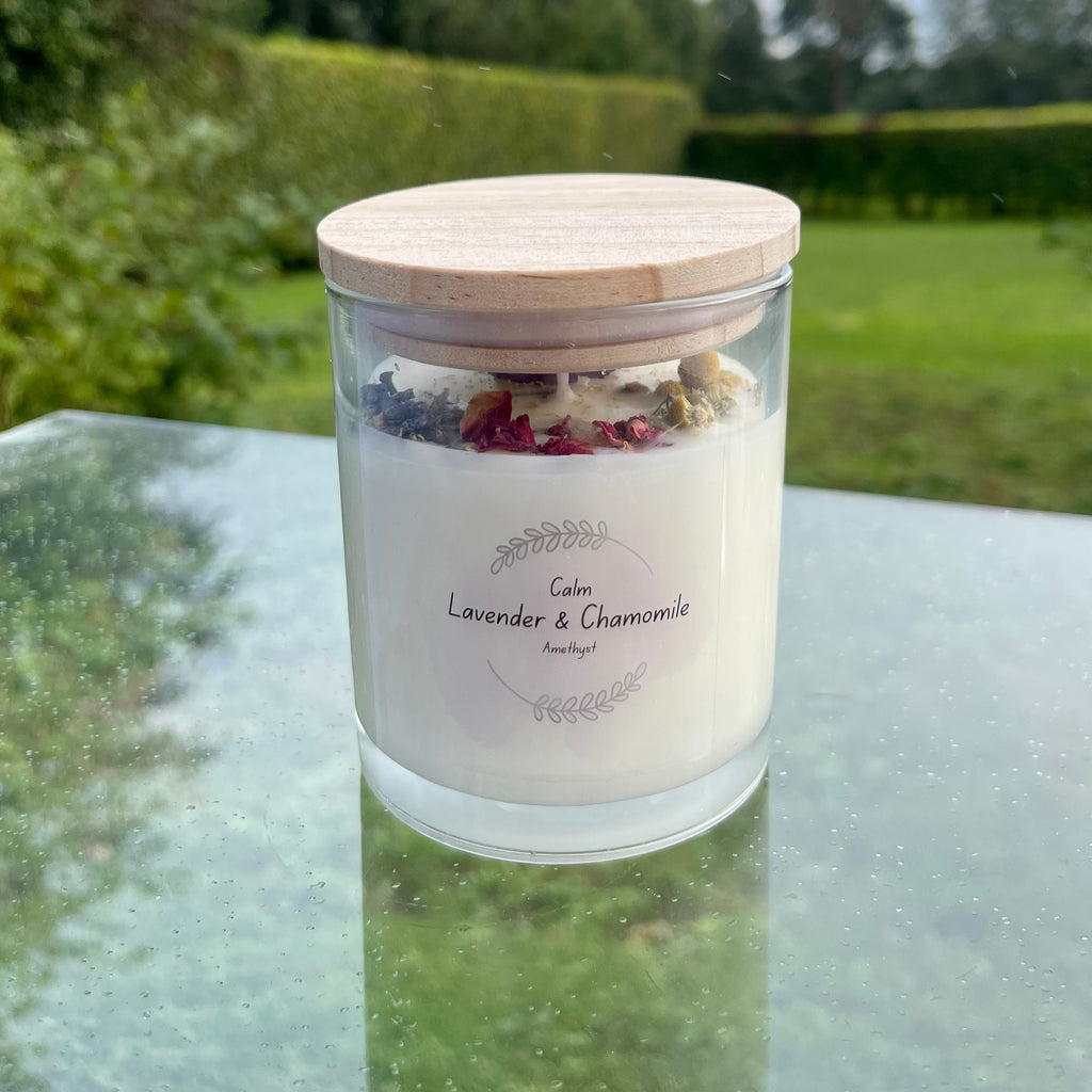 A glass jar with white soy wax inside with a rose quartz tumblestone and rose petals set in the top. the jar has a bamboo lid.
