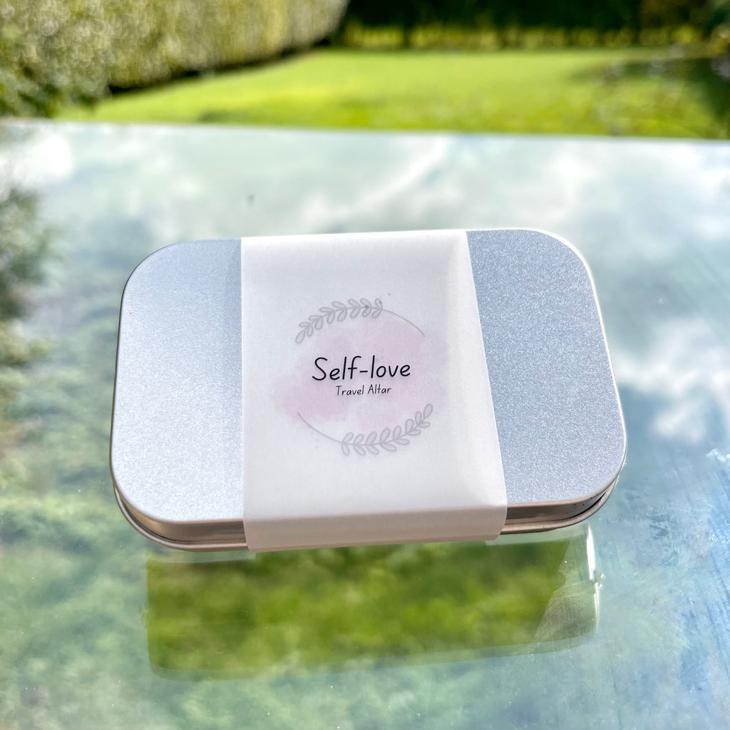 a sealed self love travel altar in a metal tin and a paper wrap